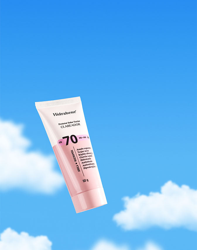 Mão segurando a bisnaga do Protetor Solar Facial FPS 70 Clareador contra o céu azul.